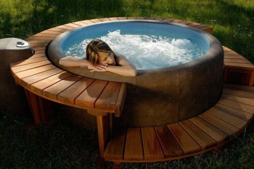 Eine Frau die im Softub Sportster Whirlpool mit Holzumrandung sprudelt